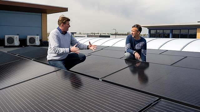 Twee mannen op een dak met zonnepanelen. De leverancier (links) legt aan Leander (rechts) uit hoe de PVT-installatie werkt. (foto: Ralph Schmitz)
